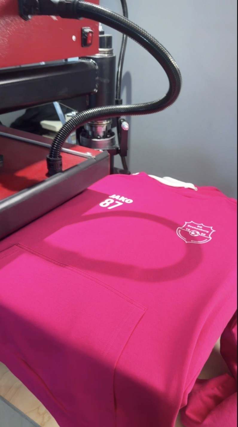 Pinker Hoodie mit Vereinslogo auf einer Transferpresse