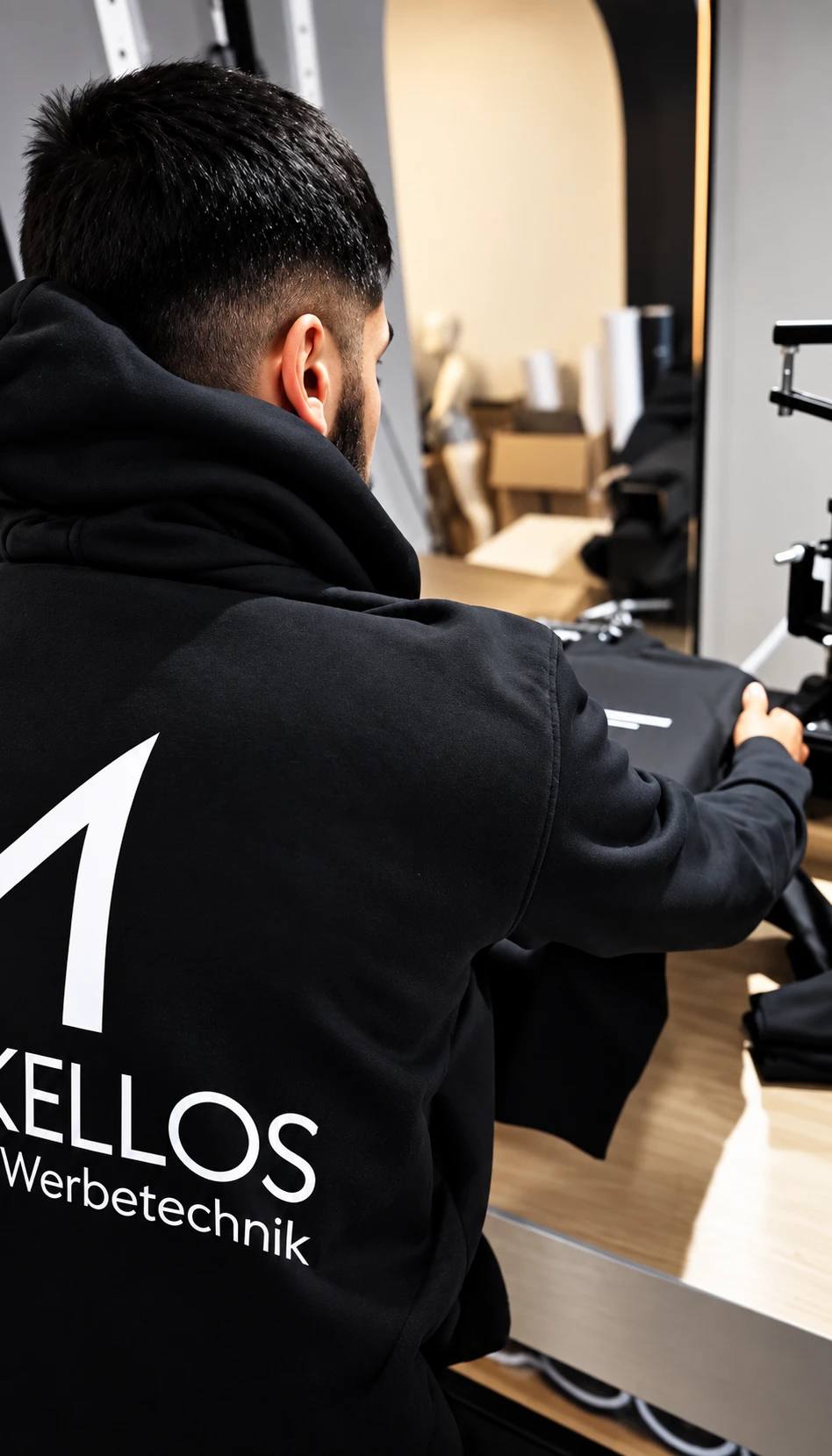 Mitarbeiter im schwarzen Firmen-Hoodie arbeitet an einer Textilpresse.