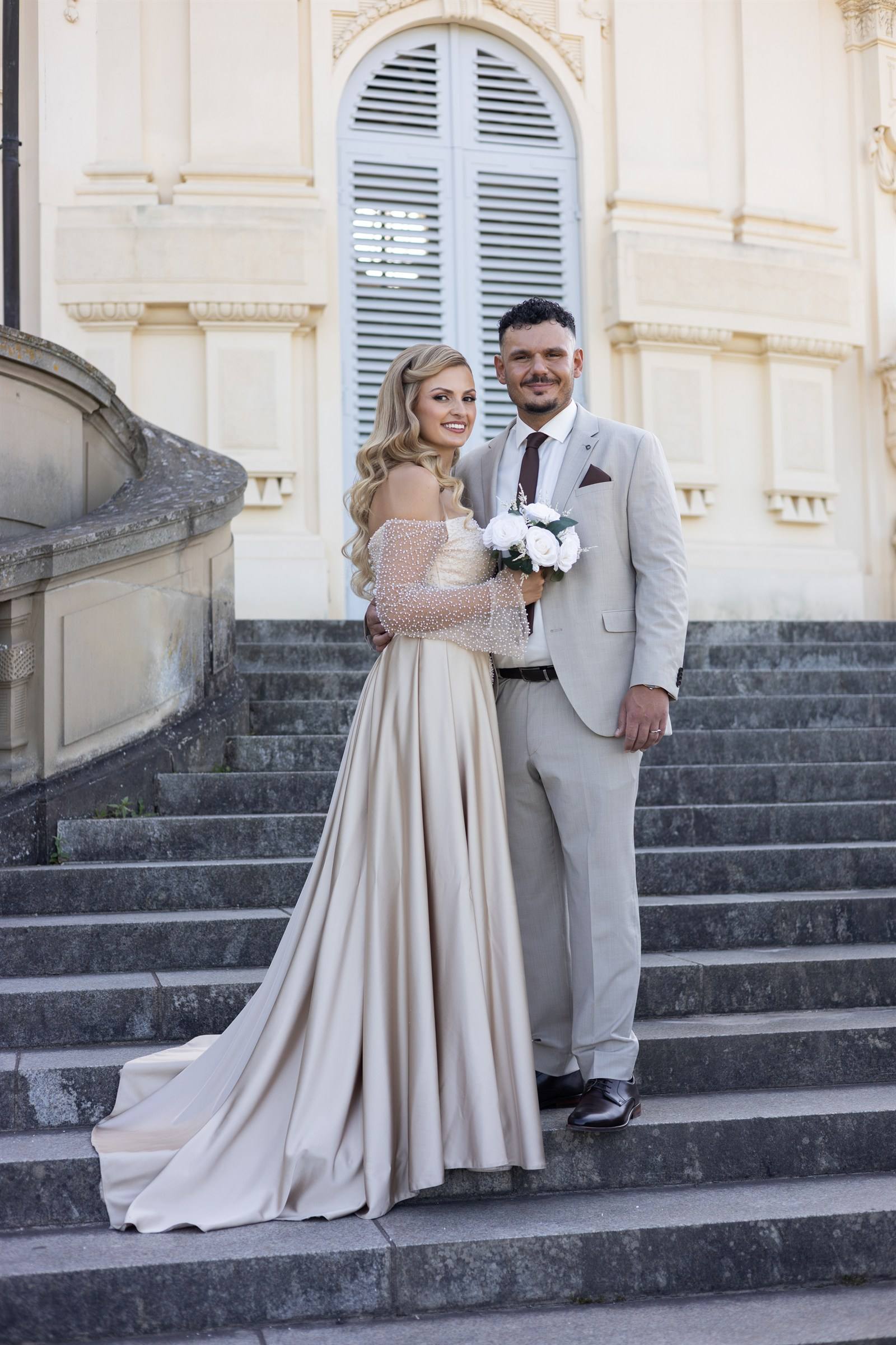 Paar auf einer breiten Schlosstreppe, sie in langem Kleid mit Schleppe